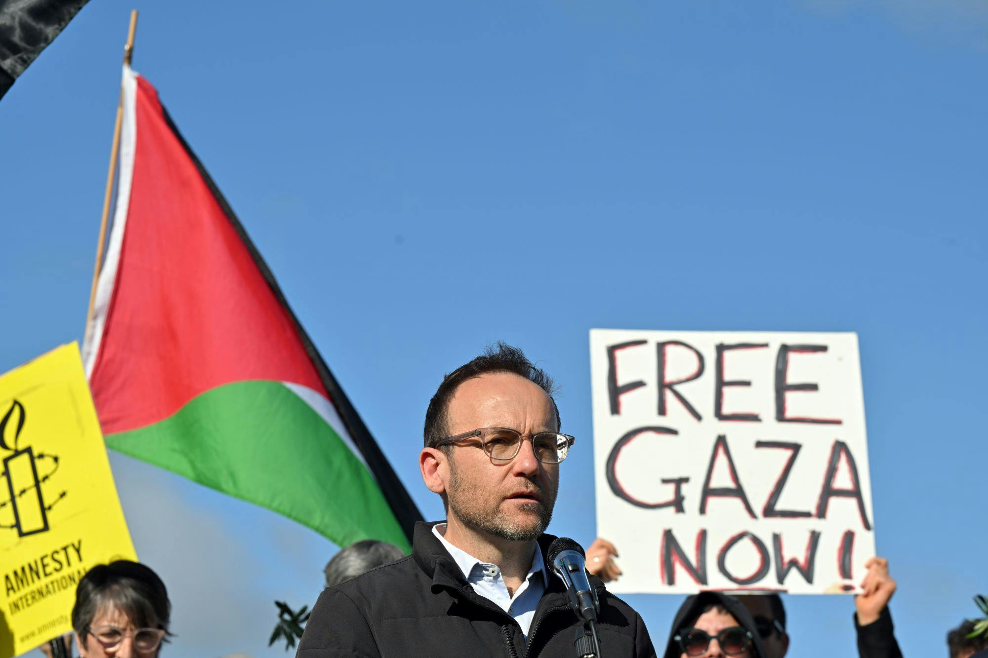 Man in front of a flag and poster reading "Free Gaza now"