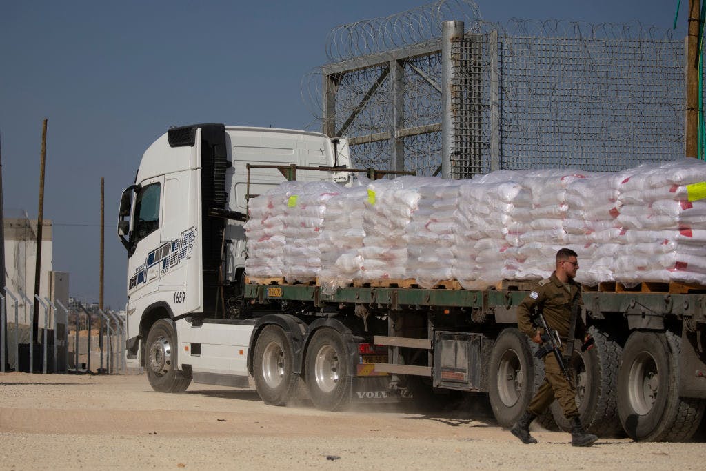 Man in uniform in front of truck laden with sacks.